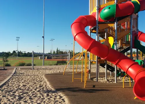 Colorful red tube slide anchors the playground with ball fields visible behind