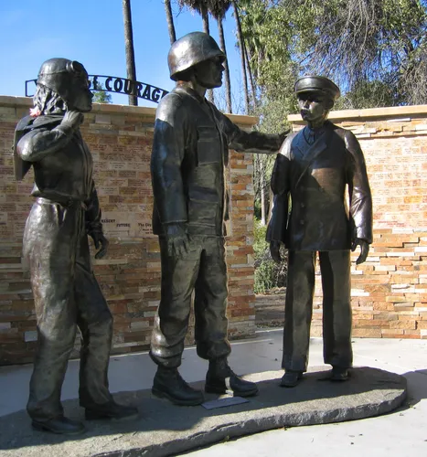 Bronze statues of three military service members standing before the Wall of Courage