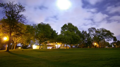 An evening view of the park lit by warm lamps under a blue twilight sky