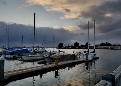 Sailboats are moored along the park's dock with dramatic cloud cover at dusk