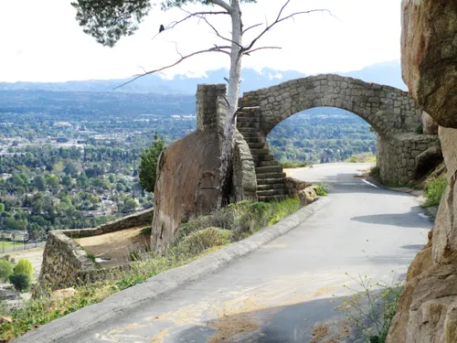 Stone arch bridge spans across the mountain road with valley views below