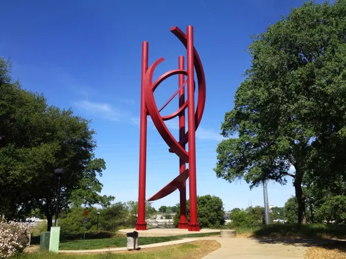 The vibrant red steel curves of the 80-foot Cosmos sculpture framed by trees