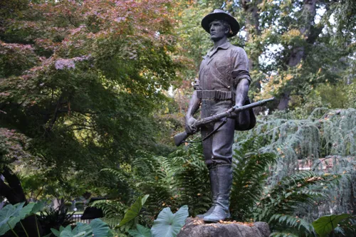Spanish American War Hiker statue stands among lush greenery