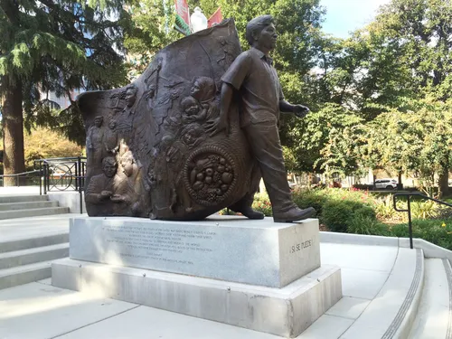 Bronze Cesar Chavez Memorial statue stands on a marble base amid greenery