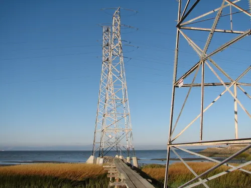A wooden pier leads out into San Francisco Bay toward a pair of transmission towers