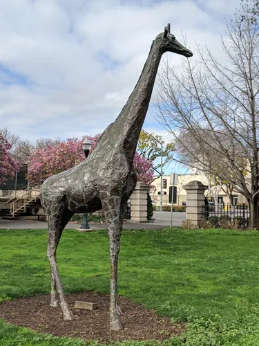 Giraffe sculpture stands on grassy area near the park's north corner