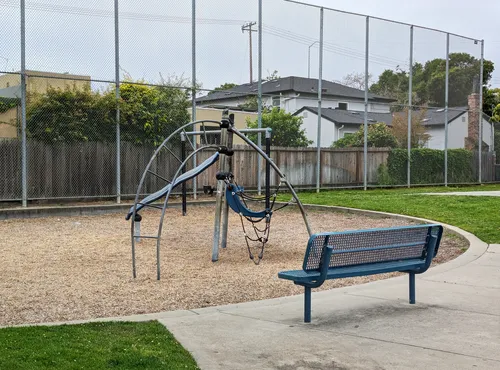 A climbing structure and blue bench sit at the playground area