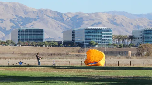 Man with orange parasail in front of mountain backdrop.