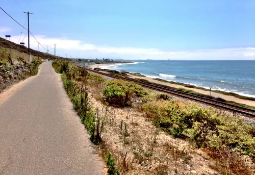 Narrow paved road runs alongside train tracks with ocean views