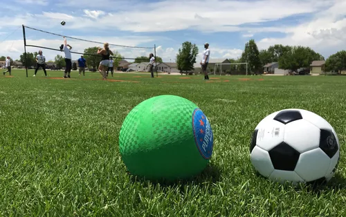 Two balls rest on the grass with a volleyball game underway in the background