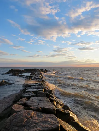 Stone breakwater extends into choppy waters under blue sky