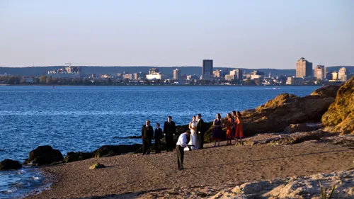 A wedding party enjoys the rocky beach with city views in distance