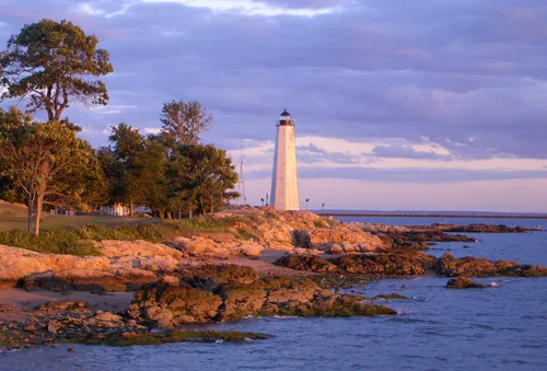 Warm sunset illuminates the lighthouse and rocky coastline