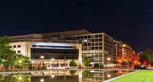 A nighttime view of the park's reflecting pool with illuminated buildings behind