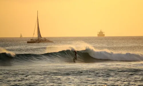 Surfer riding waves in golden waters at sunset