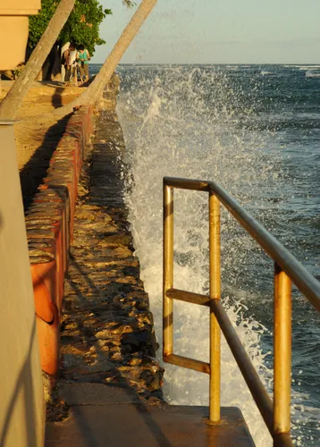 Waves splash against the seawall in golden sunset light