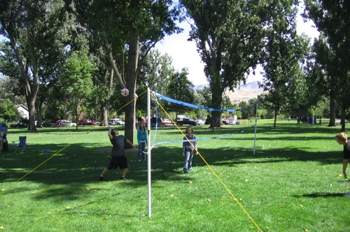 Kids playing volleyball in the grassy recreation area under shade trees
