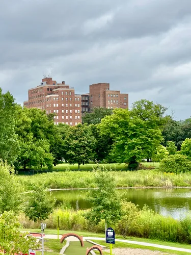 A pond and lush greenery frame a red brick building in the background