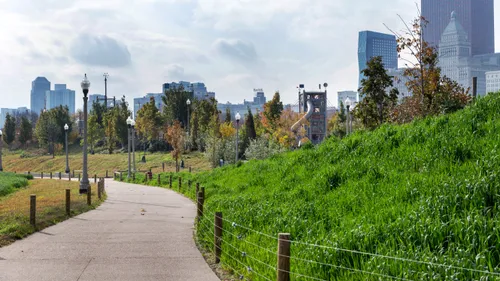Curving walkway bordered by lush grass slopes and downtown skyscrapers