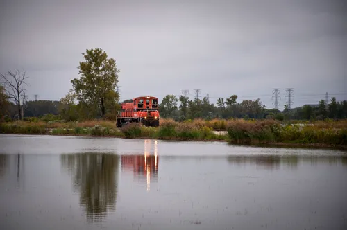A red locomotive passes alongside the lake at the recreation area