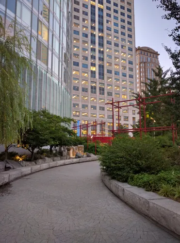 The serpentine walkway leads toward red sculptural elements and downtown towers