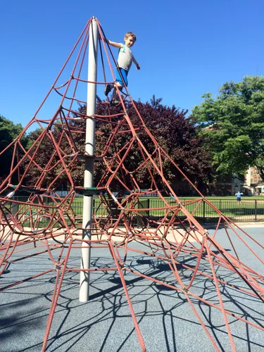 A child explores the rope pyramid structure at the park's playground