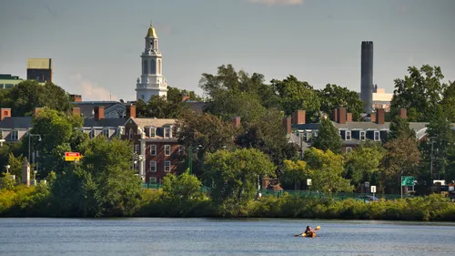 Harvard Business School campus visible through riverside foliage