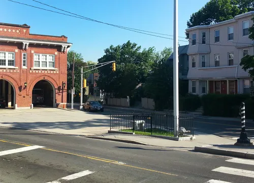 The adorable park with its bench and flagpole sits in front of a firehouse building