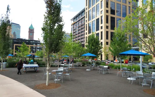 Urban seating area with blue umbrellas and tables along the park's north edge