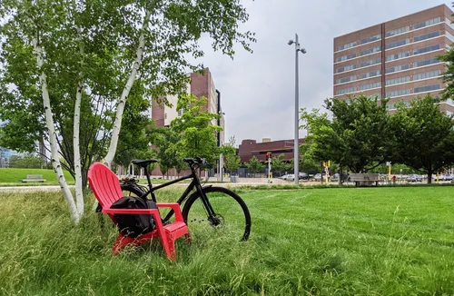 A bike is parked next to a red chair in the greenspace