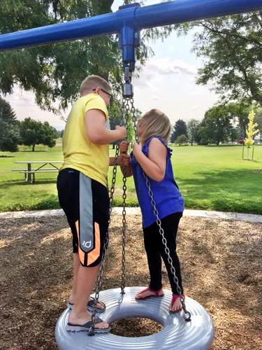 Two kids at the playground with the green park grounds behind