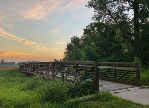 A wooden footbridge curves through the green landscape at dawn