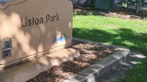 The Liston Park entrance sign sits among trees and wood chip landscaping