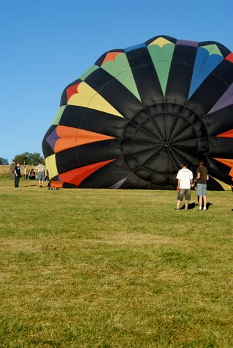 A colorful hot air balloon is being inflated on the open grass fields of the park