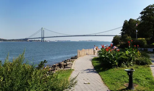 Peaceful walking path along the waterfront with Verrazzano Bridge in distance