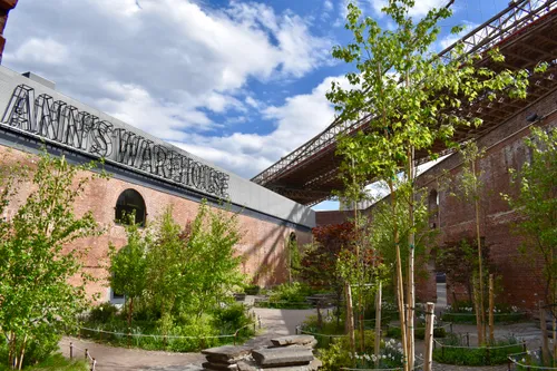 The brick facade of St. Ann's Warehouse in Max Family Garden with Brooklyn Bridge above