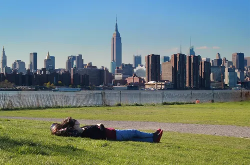 A visitor relaxes on the lawn with the Manhattan skyline visible across the water