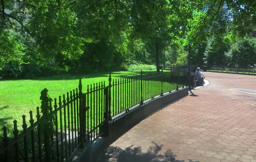 The park's wide pathway curves along an iron fence surrounded by lush green trees