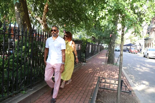 A couple strolls along the brick path beside the park's iron fence