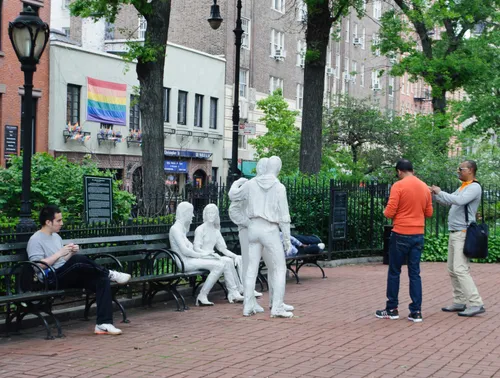 The Gay Liberation Monument with visitors nearby and a Pride flag in the background