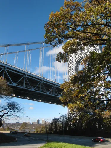 George Washington Bridge towers above the tree canopy near the riverbank