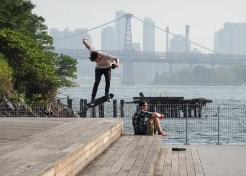With the Williamsburg Bridge visible behind him, a skateboarder launches into the air near the water's edge