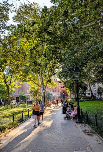 A sunlit pathway lined with trees welcomes park visitors