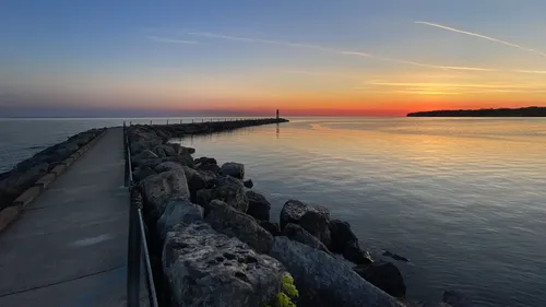 A breakwater stretches into Lake Ontario toward the distant beacon