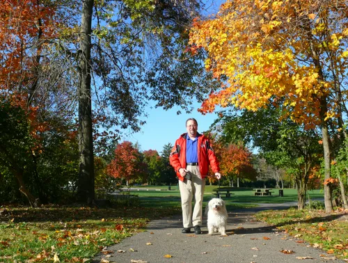 Autumn colors frame a walking path where a visitor strolls with his dog