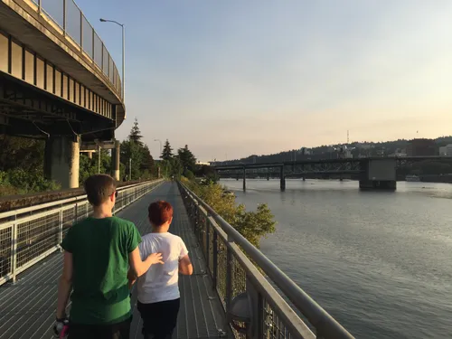 Two visitors walk along the Eastbank Esplanade with Morrison Bridge visible in the distance