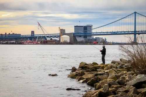Angler casting a line with Benjamin Franklin Bridge spanning the Delaware River
