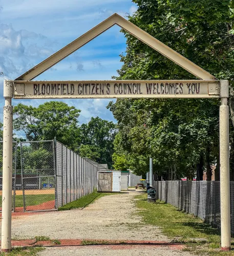 A metal welcome arch leads visitors toward the baseball field