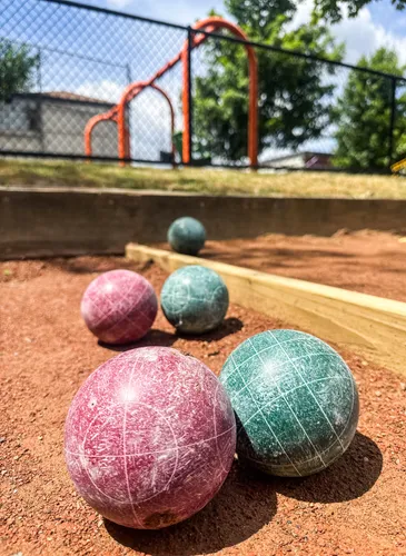 Bocce balls rest on the court's clay surface near the playground