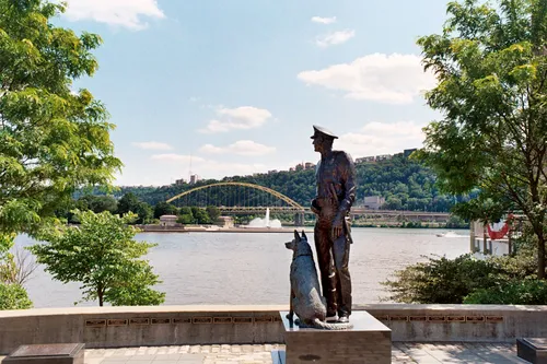 Memorial statue stands guard with Point State Park Fountain and Fort Pitt Bridge visible across the water